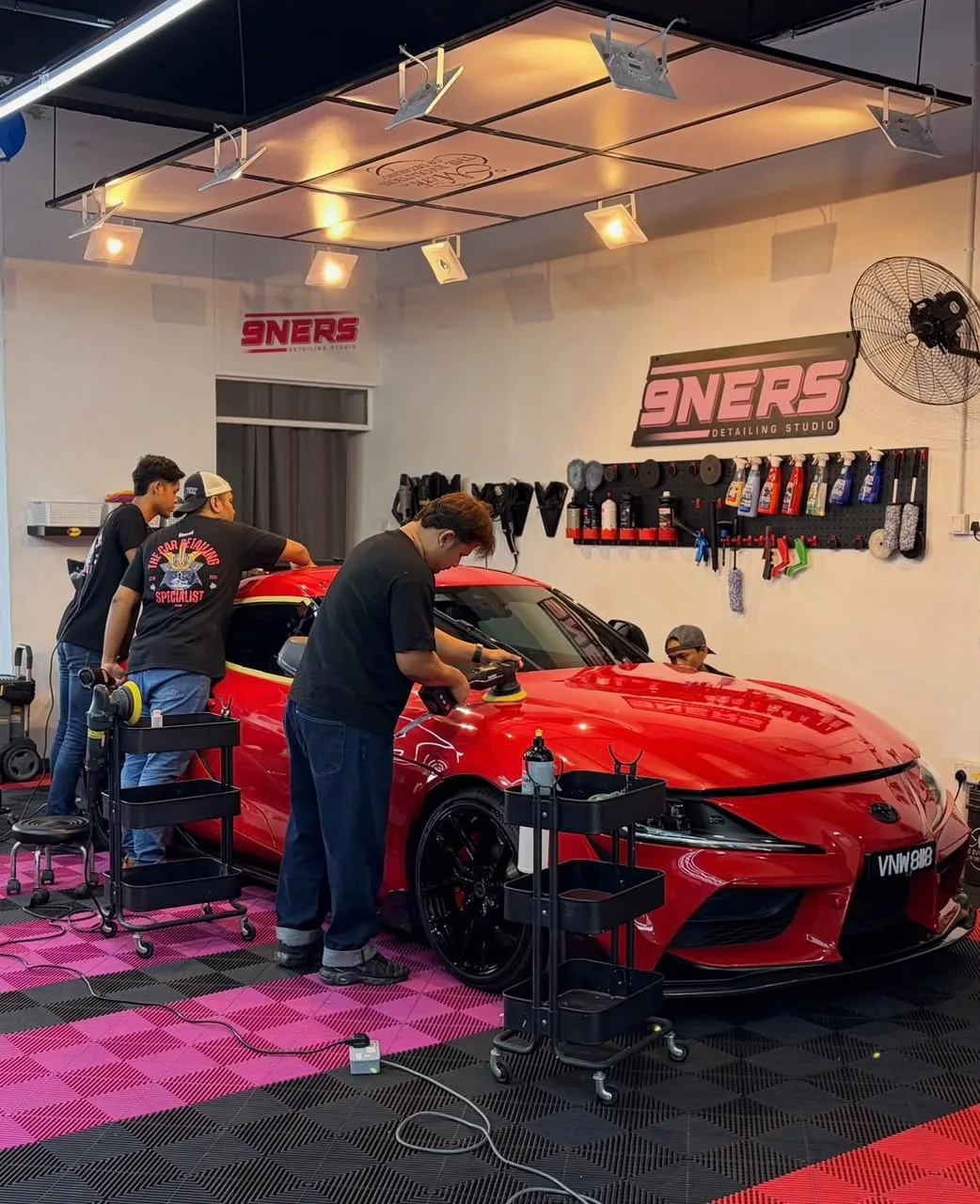The 9NERS team machine-polishing a red sports car in the studio